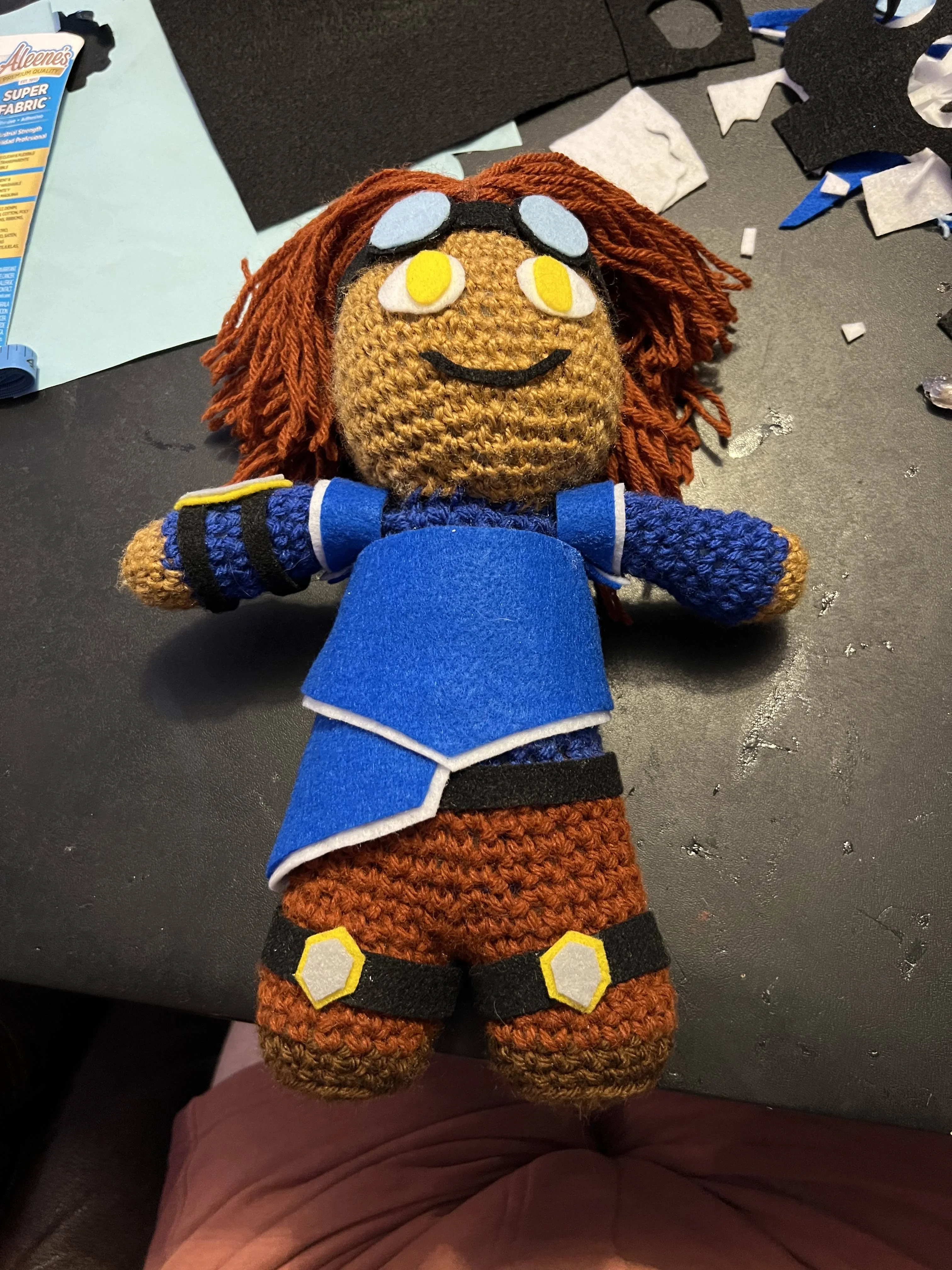 Crochet doll with brown skin, brown hair, and blue clothes
